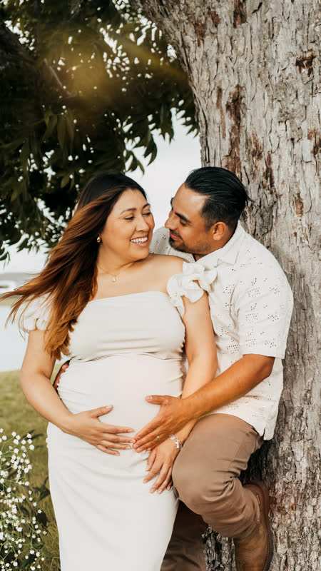 Expecting couple embracing under a tree at golden hour